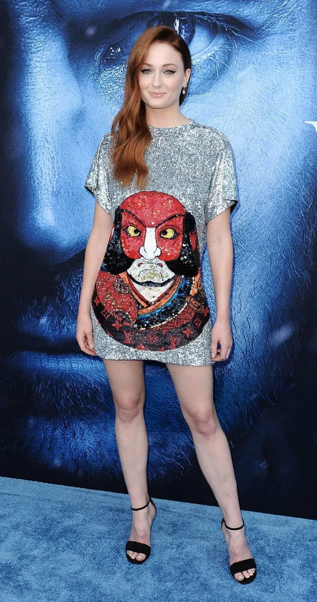 Sophie Turner posing in a patterned mini dress and black heels at a film event.
