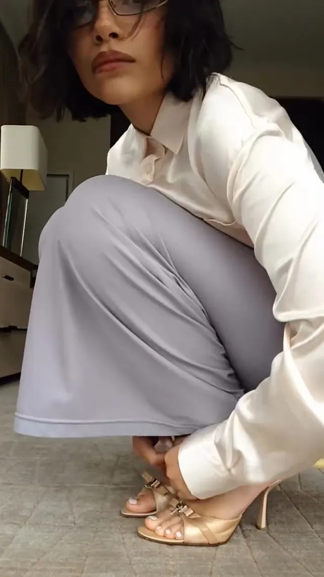 Ariana Greenblatt crouching in a pale blouse and metallic heels.