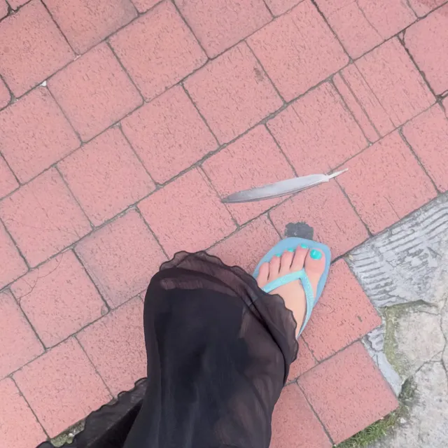 Addison Rae wearing turquoise flip-flops on a brick pavement.