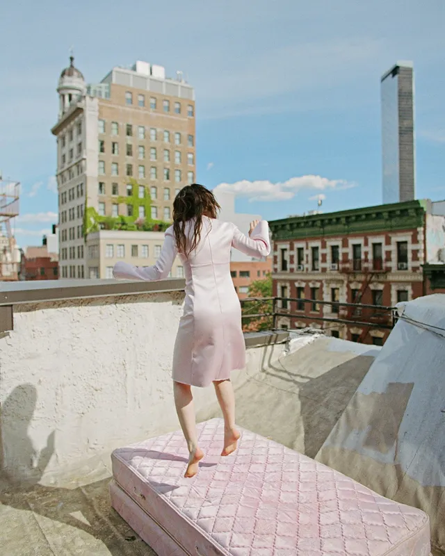Sophie Thatcher walking barefoot across a rooftop mattress.