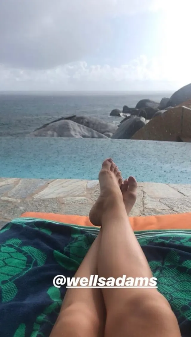 Sarah Hyland resting her feet beside a pool overlooking the sea.