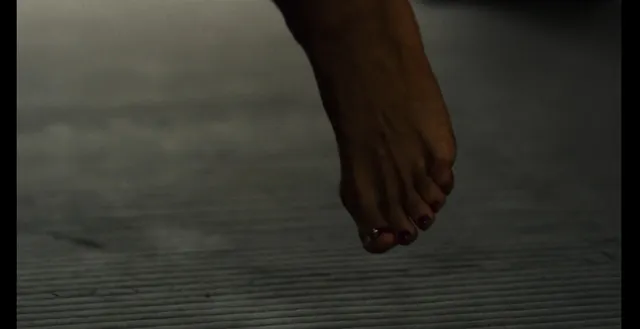 Rosario Dawson resting a bare foot in a dimly lit screen scene.