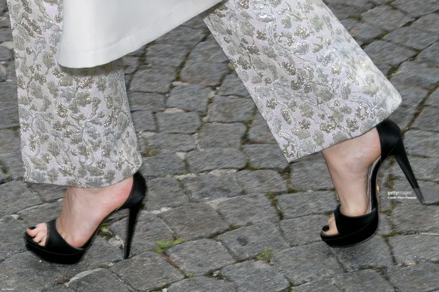 Léa Seydoux walking on cobbles in black heels.