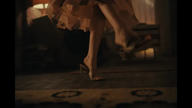 Emilia Clarke wearing strappy heels on a wooden floor.