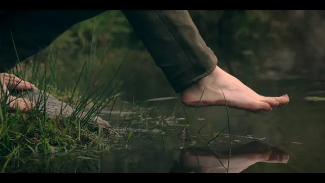 Freya Allan stepping barefoot through shallow water in a film scene.