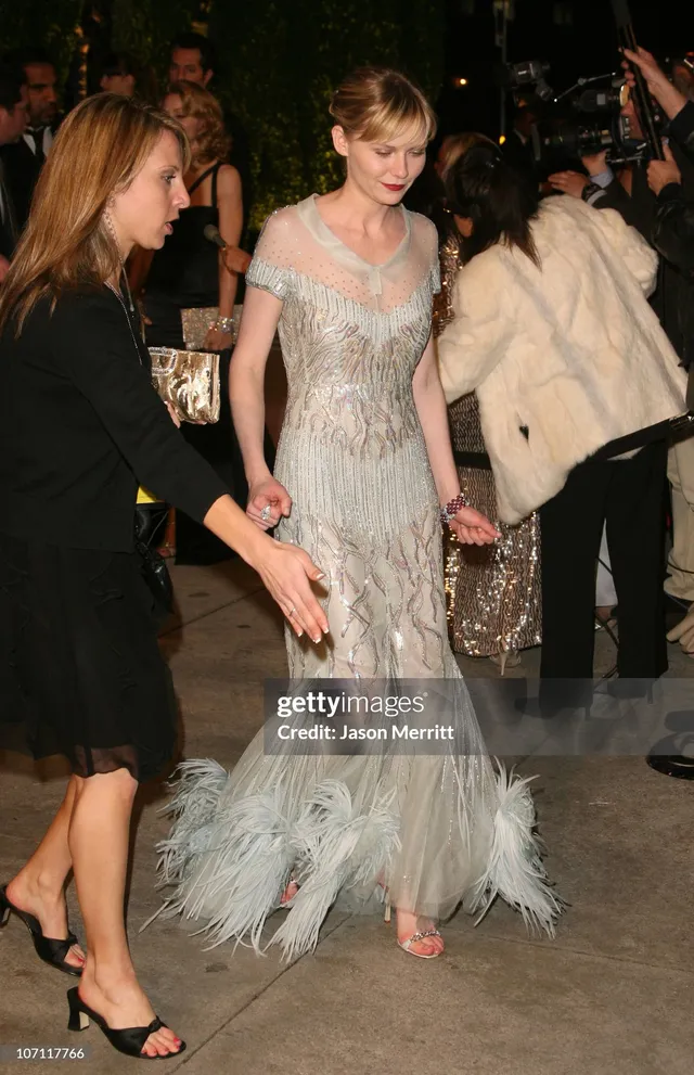 Kirsten Dunst walking at an event in a pale embellished gown.
