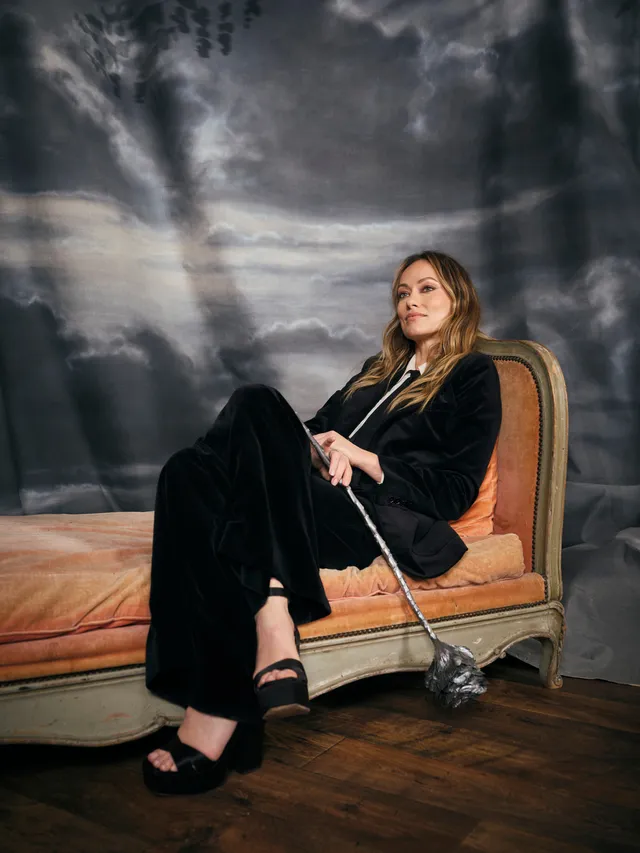 Olivia Wilde sitting in a velvet outfit and black platform heels.