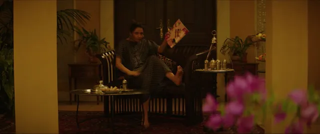Naomi Scott reclining barefoot on a chair in a screen scene.