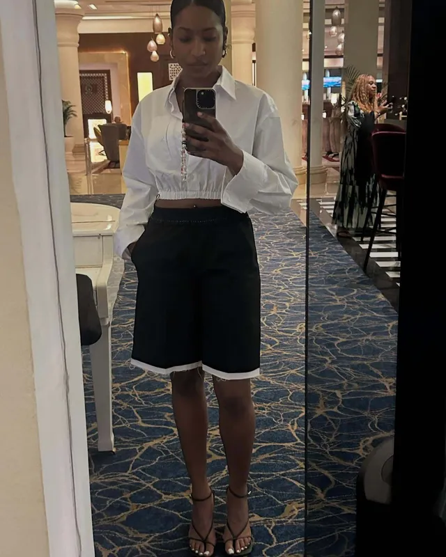 Carlacia Grant taking a mirror selfie in a white shirt, dark shorts and strappy heels.