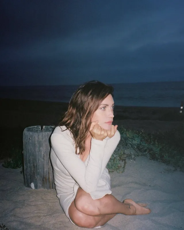 Brittany Snow sitting on sand in a pale sweater.