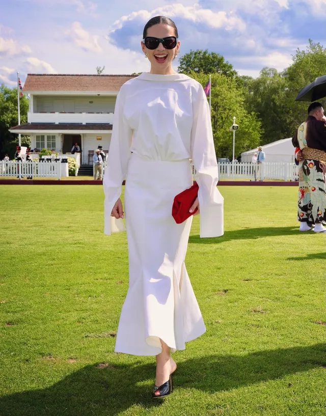Hayley Atwell walking on a lawn in a white outfit.
