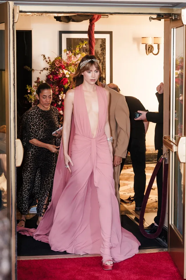 Suki Waterhouse walking through a doorway in a long pink gown.
