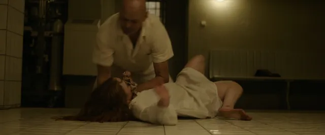 Sadie Sink lying barefoot on a floor in a film scene.