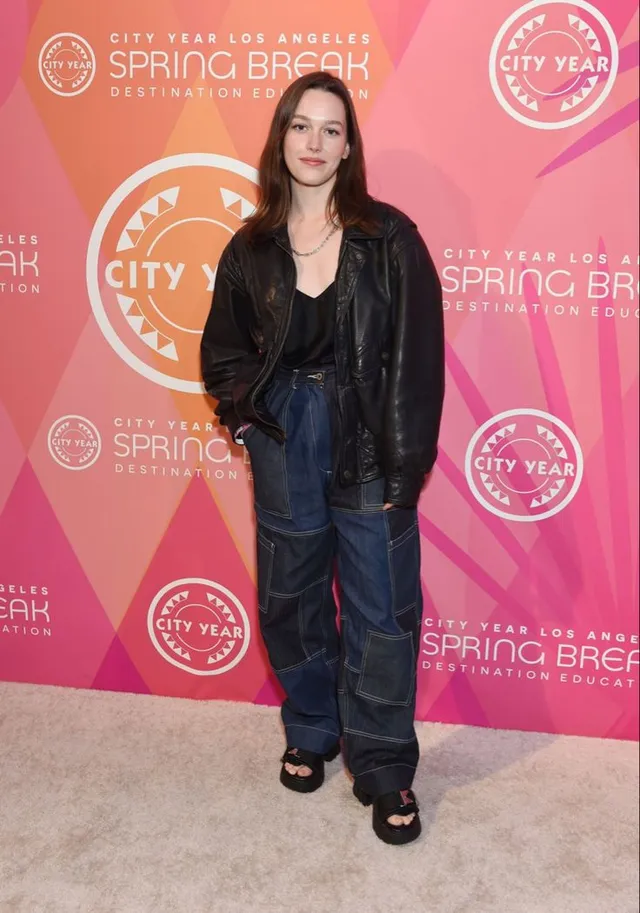 Victoria Pedretti standing at a charity event in a dark outfit.